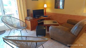Ein Wohnzimmer mit Sofa, einem Sessel, einem Fernseher, einer Lampe und einem kleinen Tisch.