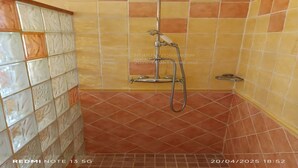 Ein Duschbereich mit gefliesten Wänden und Boden, einer Handbrause und einem wandmontierten Wasserhahn.