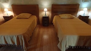 Ein Zimmer mit zwei Einzelbetten, Holz-Kopfteilen, Nachttischlampen und einem kleinen Nachttisch mit Lampe.