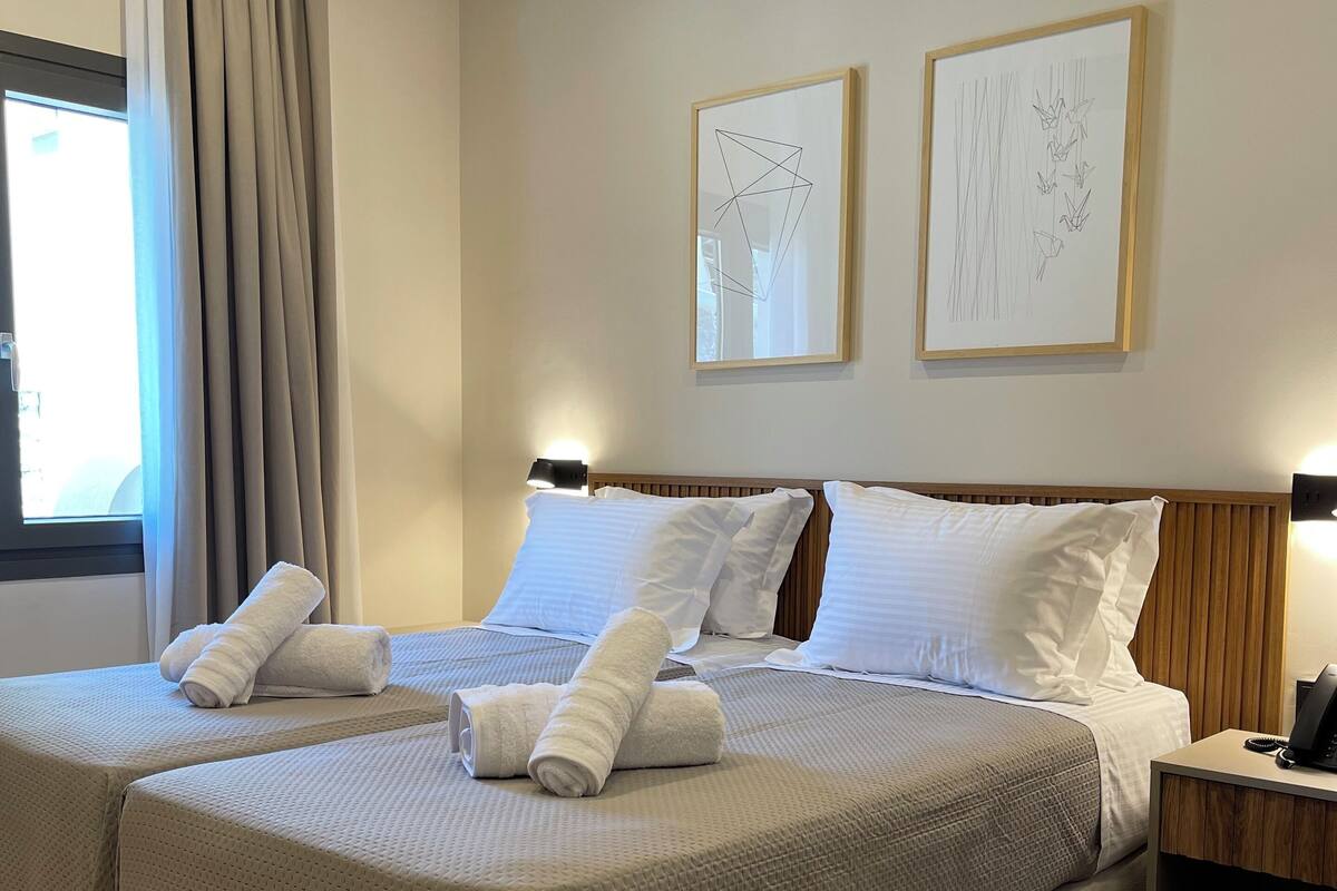 A double bed with two pillows and rolled towels, a bedside table with a phone, and two framed artworks on the wall.