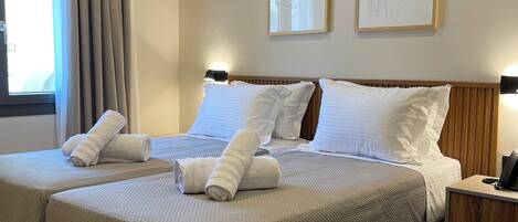 A double bed with two pillows and rolled towels, a bedside table with a phone, and two framed artworks on the wall.