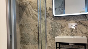 A bathroom with a glass-enclosed shower, a white sink, and a marble backsplash. - Akti Vigla Premium (Lesvos)