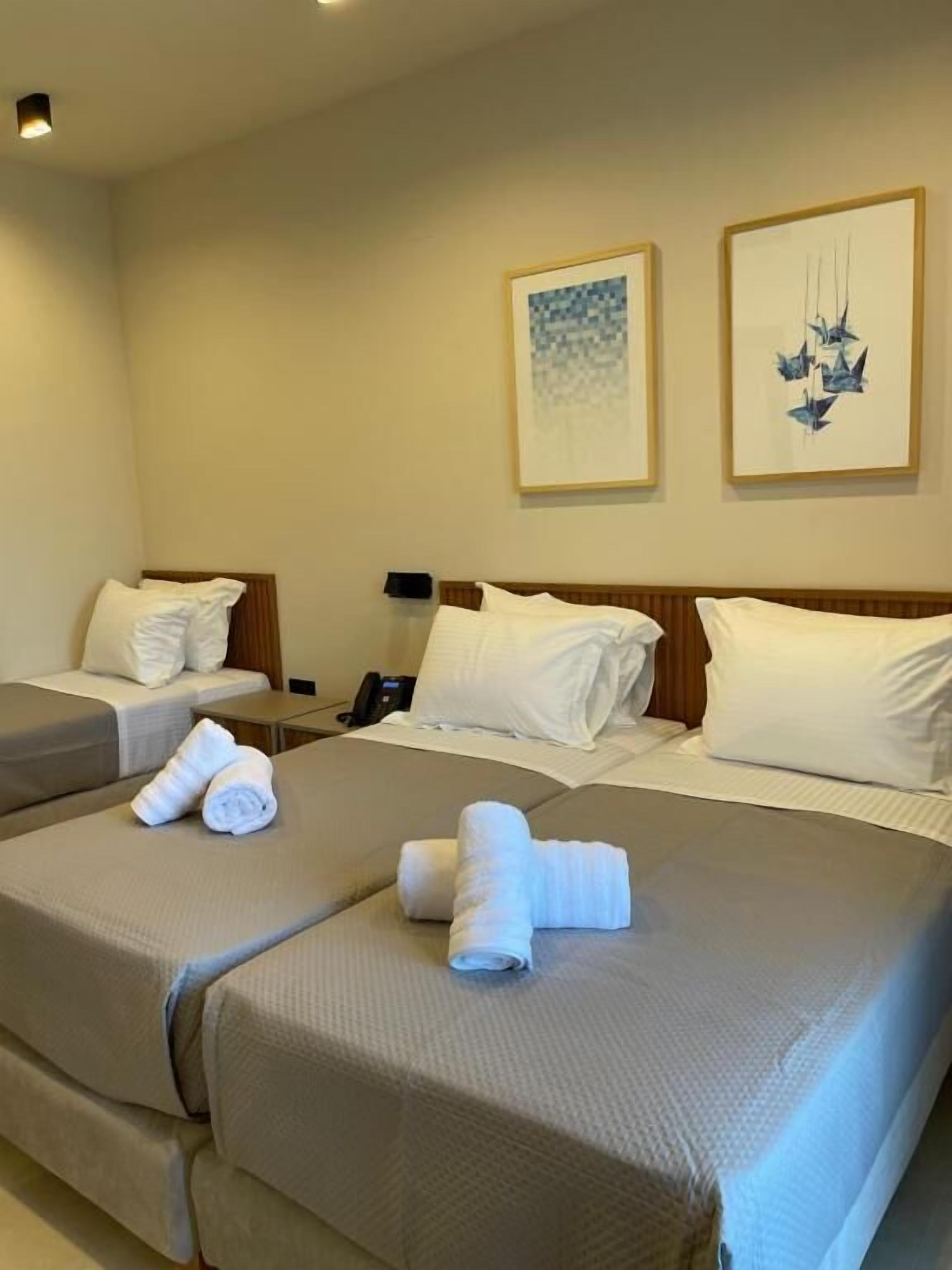 A hotel room with two beds, each with a neatly folded towel. There are two framed artworks on the wall.
