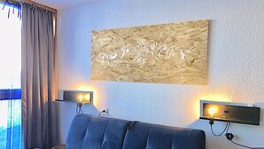 A modern living room with a dark blue sofa, two wall-mounted lamps, and a large abstract painting on the wall. - Apartment facing the slopes, ski in, ski out! Les Arcs 1800 (Bourg-Saint-Maurice)