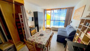 A compact living space with a dining table, chairs, a sofa, a TV, and a bookshelf. - Apartment facing the slopes, ski in, ski out! Les Arcs 1800 (Bourg-Saint-Maurice)
