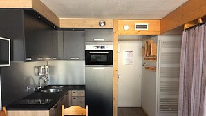 A compact kitchen with a microwave, sink, and stove, a dining area with a patterned tablecloth, and a wooden ceiling. - Apartment facing the slopes, ski in, ski out! Les Arcs 1800 (Bourg-Saint-Maurice)