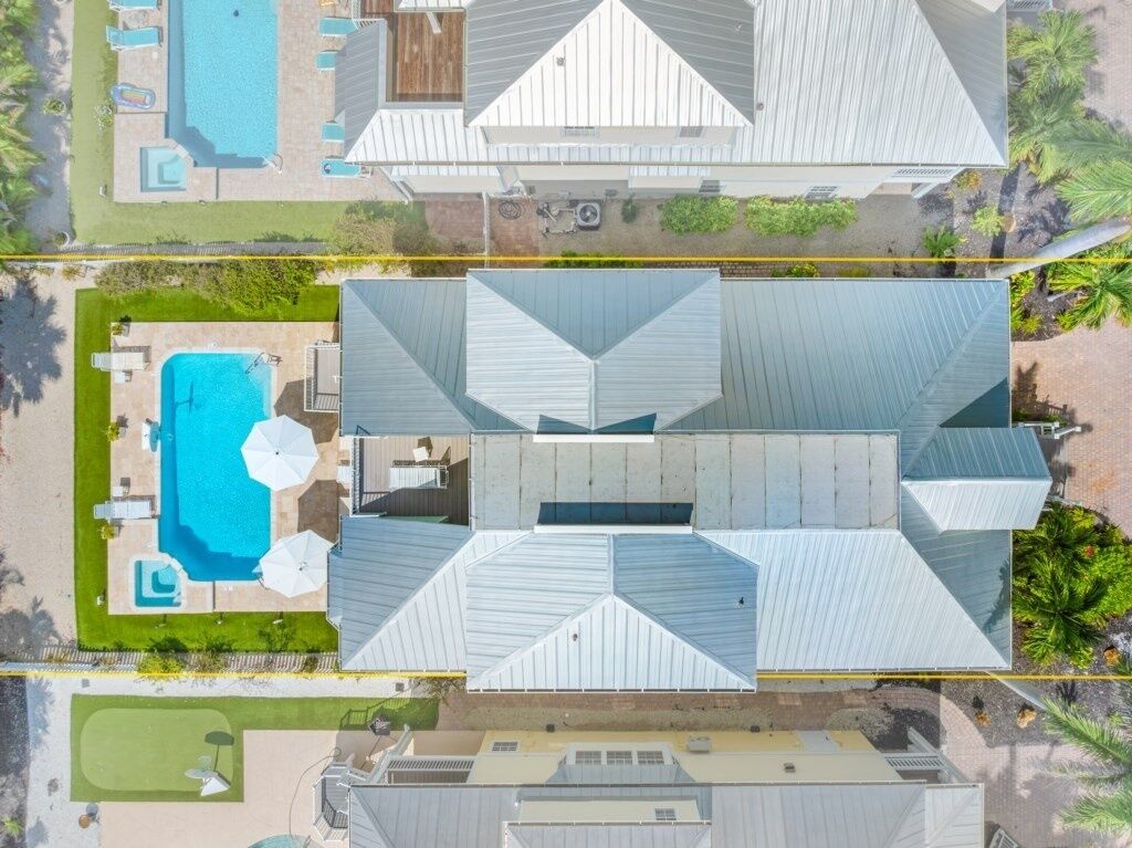 An aerial view of a property with two swimming pools, a covered patio area, and a landscaped garden.