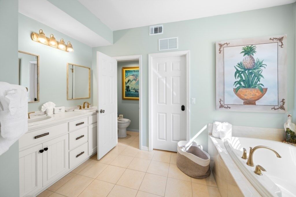 A bathroom with white cabinetry, a large mirror, a sink, a bathtub, and a painting of a pineapple.