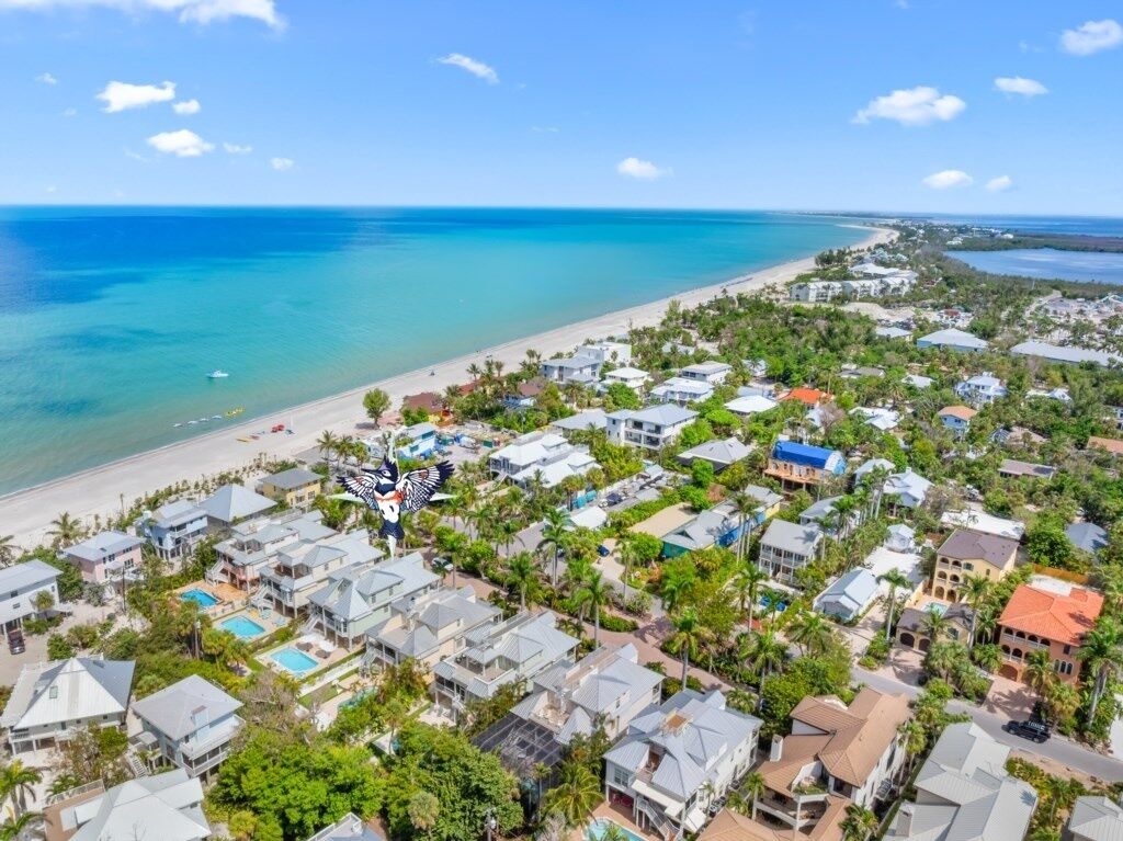 Vue aérienne d’une zone résidentielle côtière, avec des maisons, une plage et une eau d’un bleu limpide.