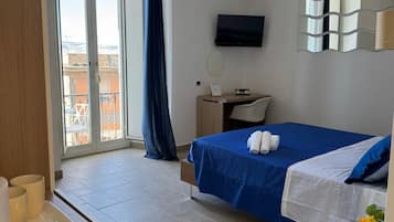 Hotelkamer met een bed, bureau, televisie en balkon met uitzicht op gebouwen.