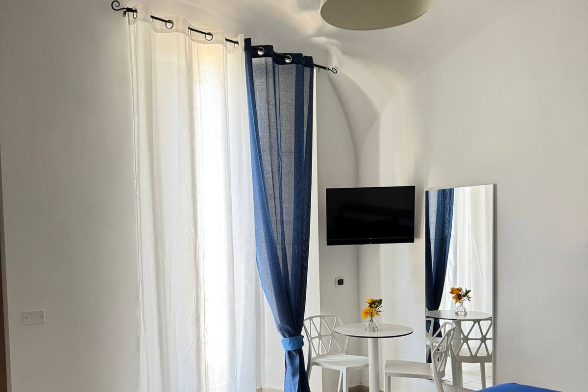 A hotel room with a bed, a desk with a chair, a TV, and a small table with a vase of flowers.