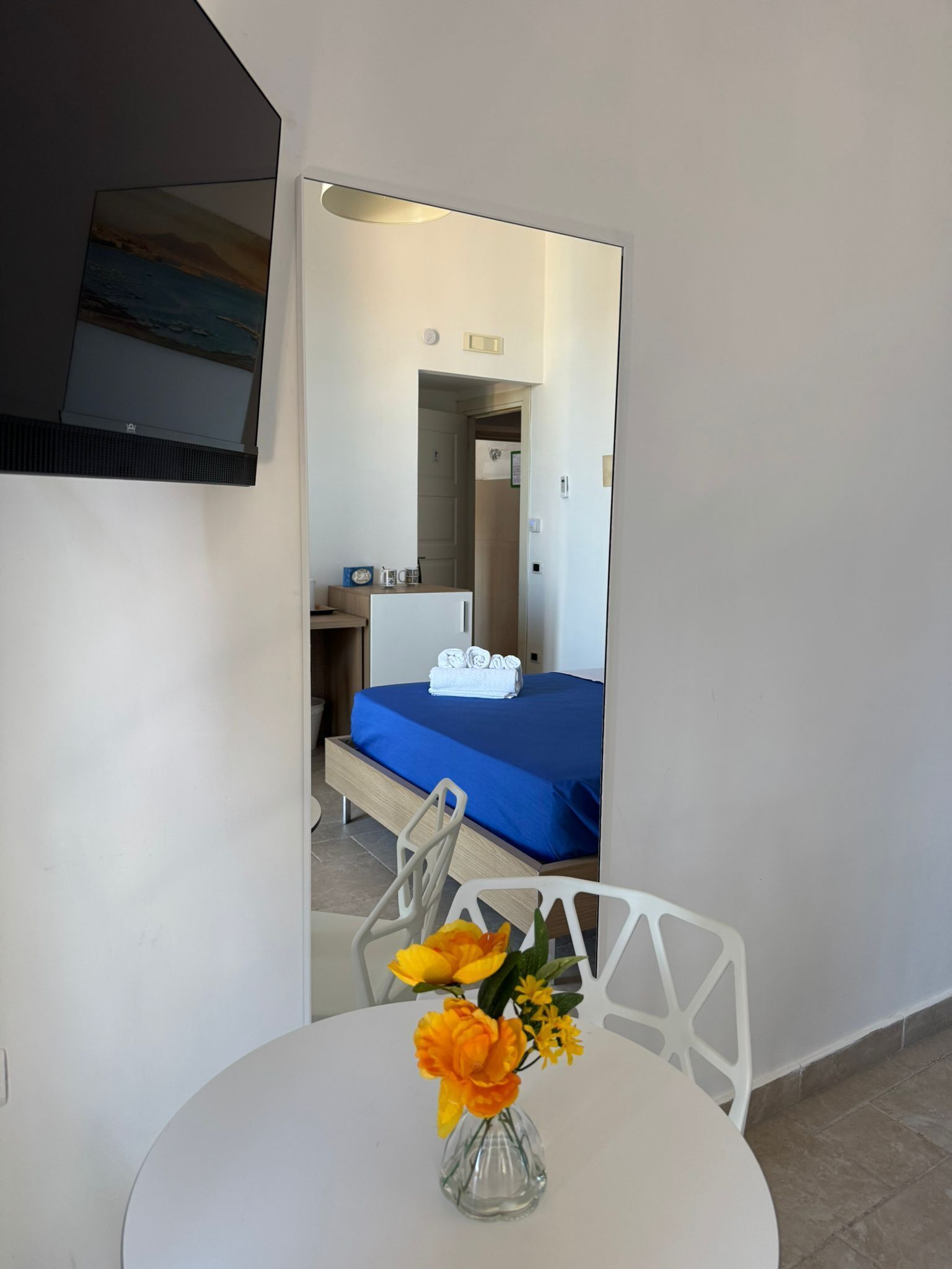 Hotelkamer met een bed, een bureau, een stoel, een bijzettafeltje met een bloevas en een aan de muur bevestigde televisie.