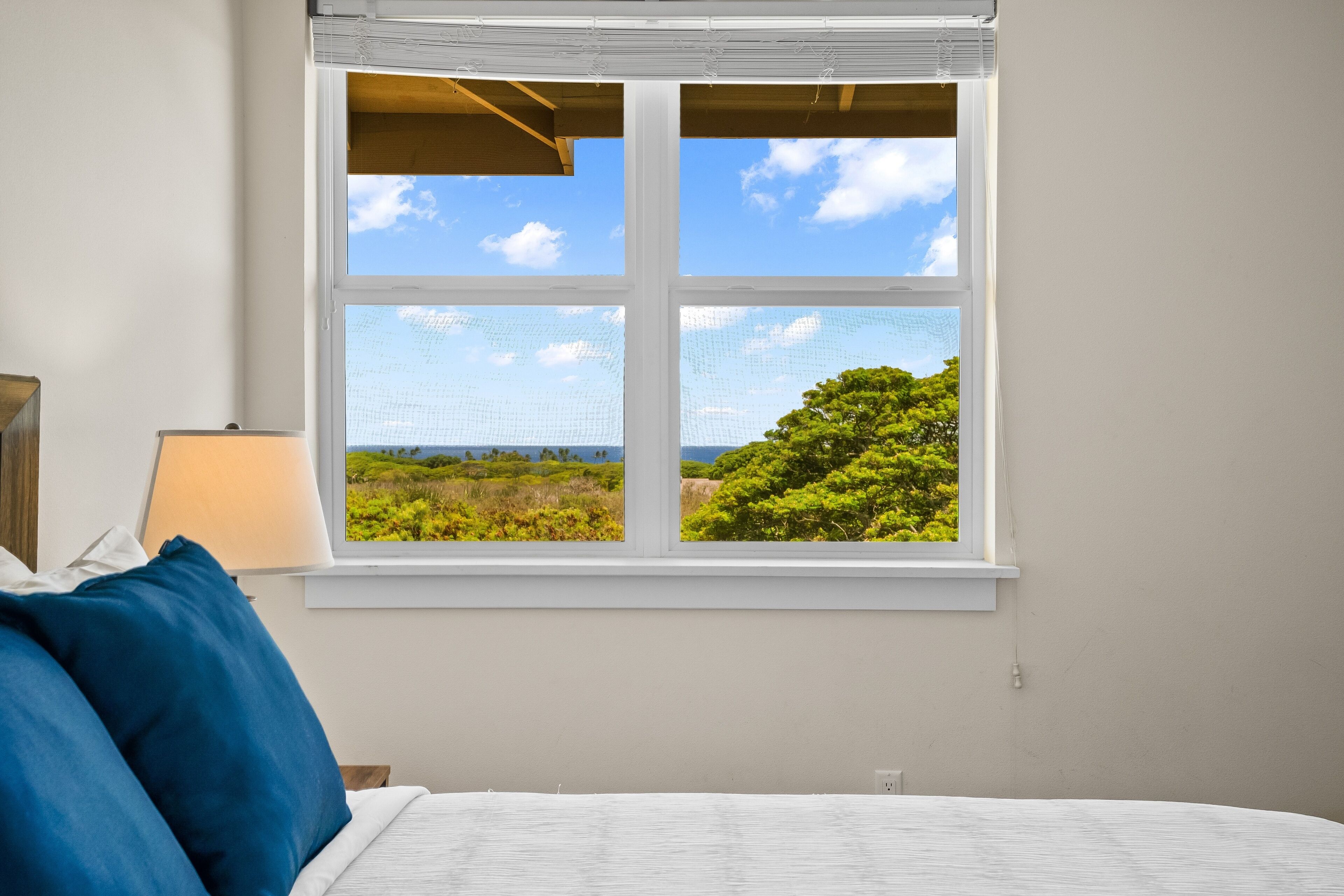 A bedroom with a large window offering a view of a green landscape and the sky.