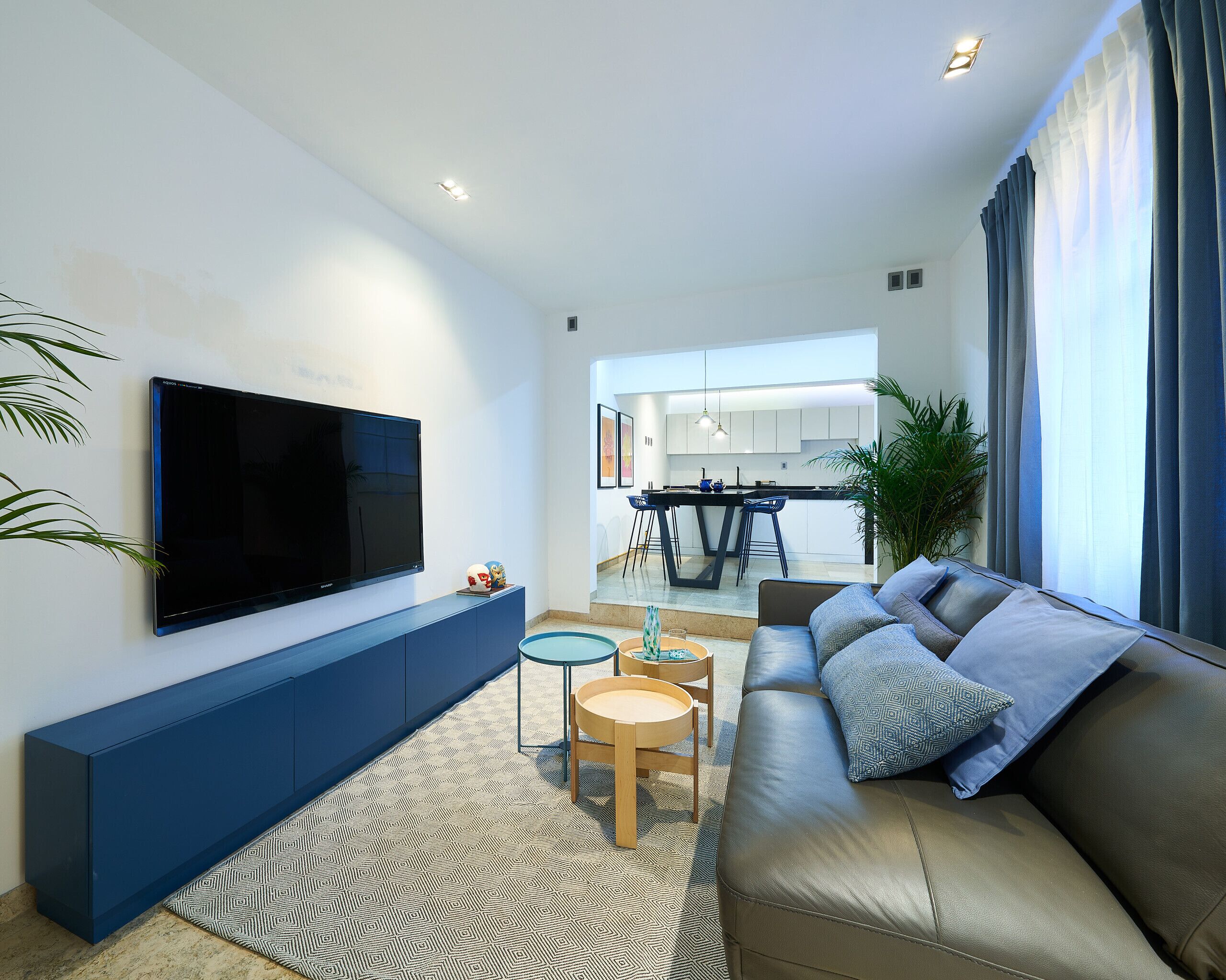 A modern living room with a large flat-screen TV, a blue sofa, a small round table, and a patterned rug.