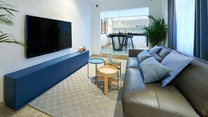 Un salon moderne avec un grand téléviseur à écran plat, un canapé bleu, une petite table ronde et un tapis à motifs.