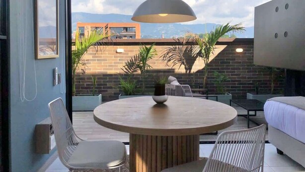 A modern outdoor patio with a round table, white chairs, and a hanging light fixture.