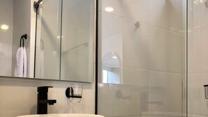 A modern bathroom with a large white vessel sink, a black faucet, and a glass shower enclosure.