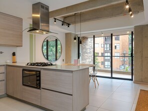 Une cuisine moderne dotée d’un îlot central, d’une hotte en acier inoxydable et de grandes fenêtres offrant une vue sur le paysage urbain.