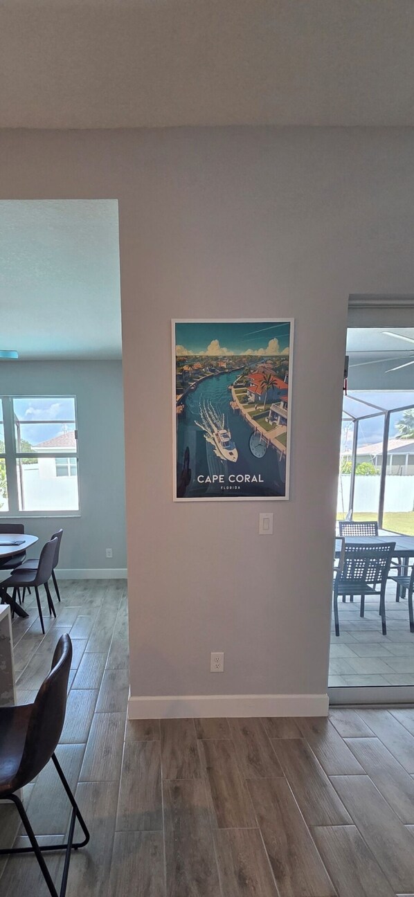 Una habitación con comedor, un ventanal grande y una obra de arte en la pared que representa una escena costera.
