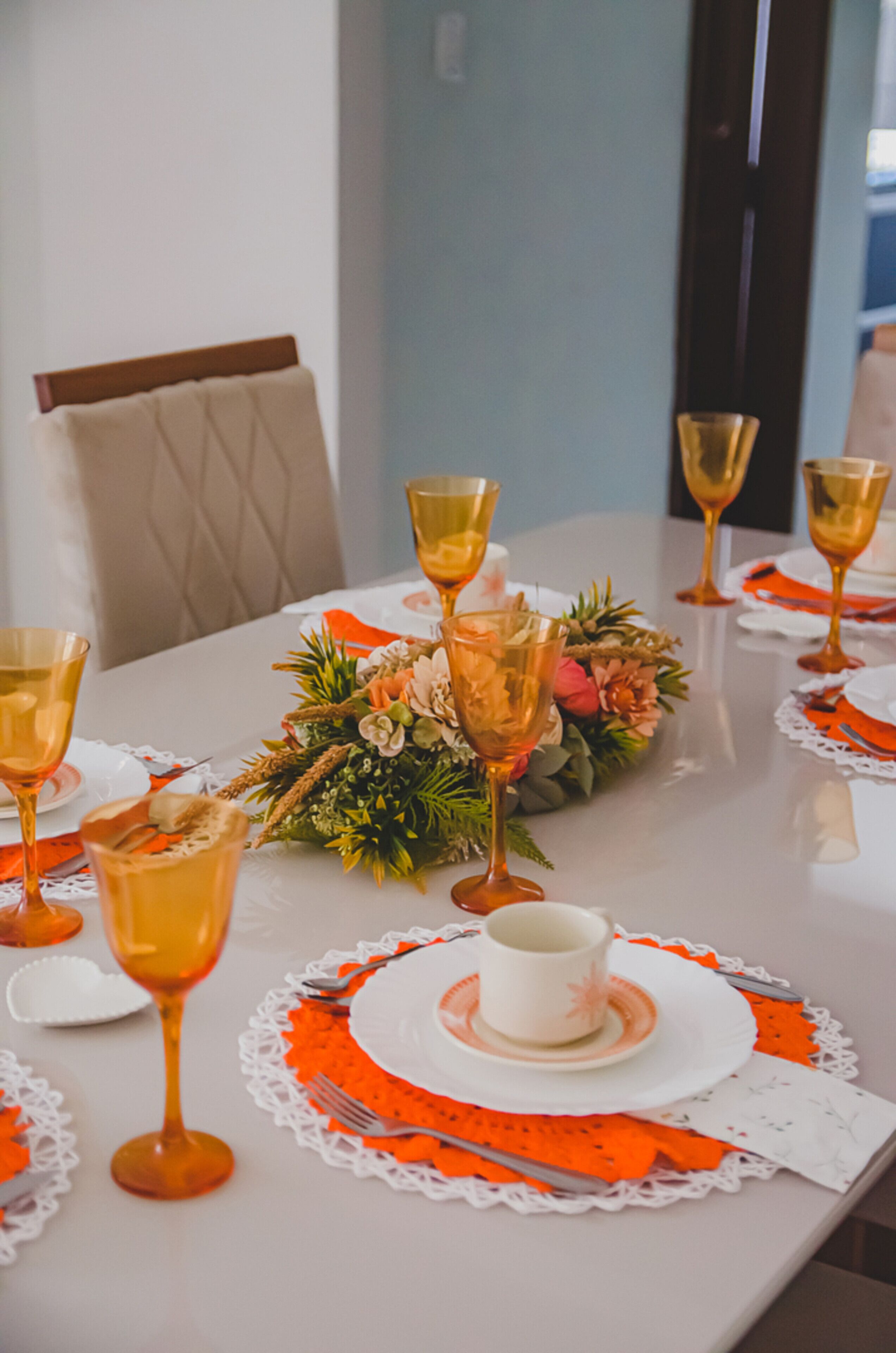 Une table à manger dressée avec de nombreux verres à vin, un centre de table composé de fleurs et des sets de table orange.