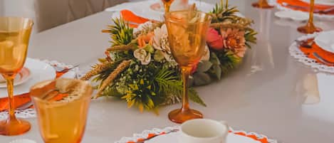 A dining table set with multiple wine glasses, a centerpiece of flowers, and orange placemats.