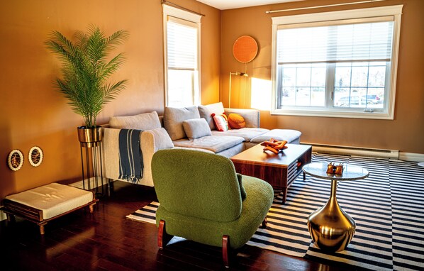 A living room with a sofa, a green armchair, a small table, a floor lamp, and a potted plant.