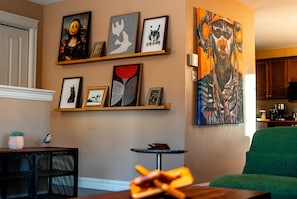 A living room with a green sofa, a small round table, and a wall decorated with framed artwork.