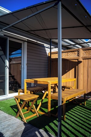 A patio with a wooden table and chairs, a covered area, and a wooden fence.