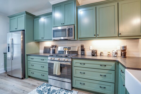 Una cocina moderna con armarios verdes, electrodomésticos de acero inoxidable y una isla central.