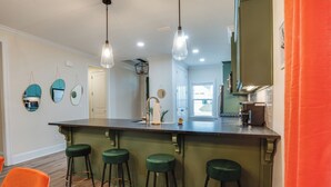 A kitchen with a bar area, green bar stools, and pendant lighting.