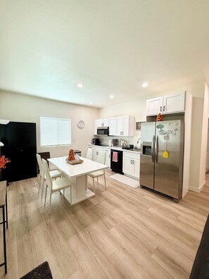 A modern kitchen with white cabinets, a stainless steel refrigerator, and a dining area with a white table and chairs. - Sheppard 2b2b Backyard ASUTempScottsd NEW (Tempe)