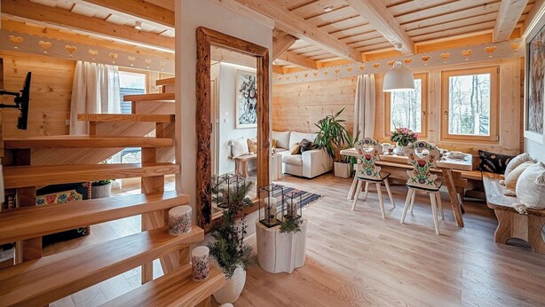 Un interior de madera con sofá, mesa de comedor y sillas, un espejo grande y una escalera con barandillas de madera.
