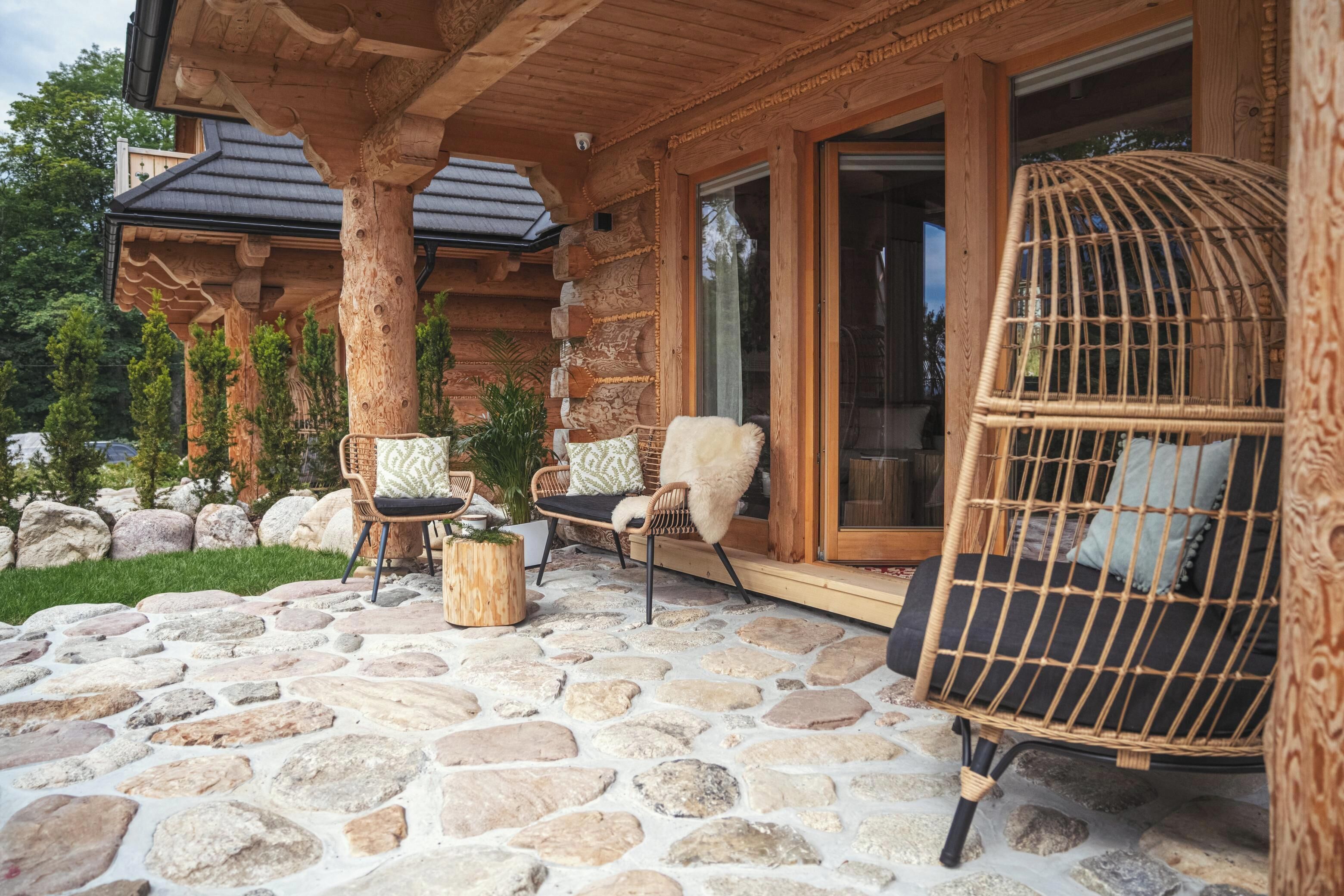 A log cabin with stone flooring, wicker chairs, and a wicker swing chair.