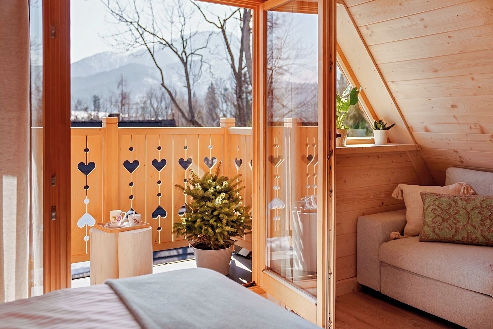 A cozy cabin room with a bed, a small table, a potted plant, and a wooden deck with heart-shaped decorations.