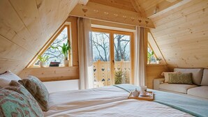 Un dormitorio acogedor en el ático, con una cama grande, un sofá y una ventana con vistas a árboles.