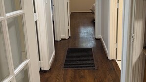 A hallway with wooden flooring, white doors, and a window with blinds.