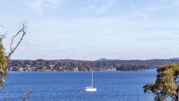 A lake with a sailboat, surrounded by trees and a distant shoreline with buildings.