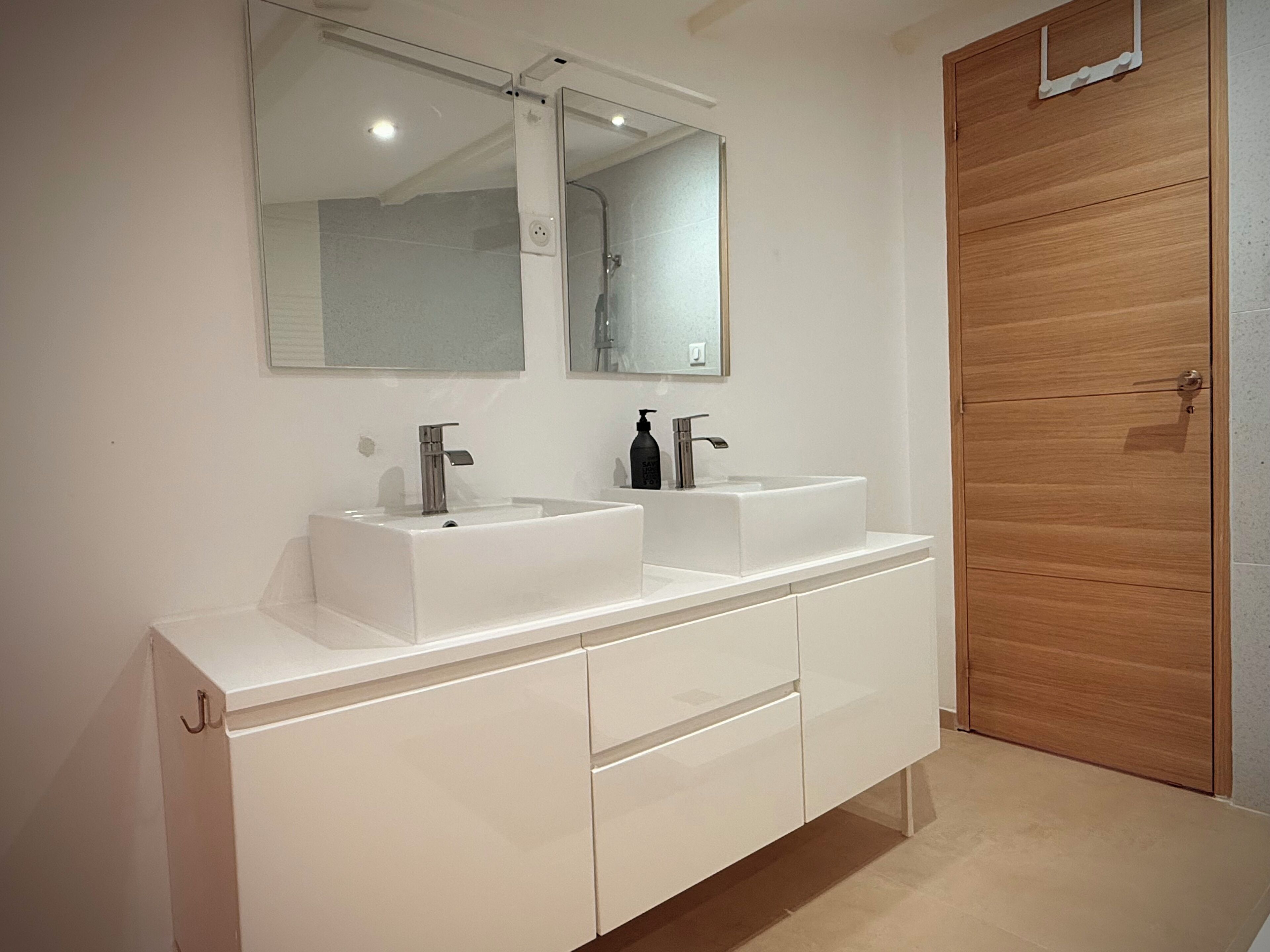 A modern bathroom with two sinks, a large mirror, and a wooden door.