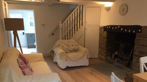 A cozy living room with a white sofa, a fireplace, and a staircase leading to another room. - The Most Beautiful and Cosy House (Kingsbridge)