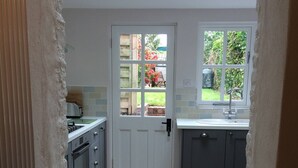 A compact kitchen with a white door, a window, and a view of the garden. - The Most Beautiful and Cosy House (Kingsbridge)