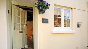 A cottage entrance with a green door, a small step leading to the door, a hanging flower basket, and a sign reading "Paul Berry Cottage". - The Most Beautiful and Cosy House (Kingsbridge)