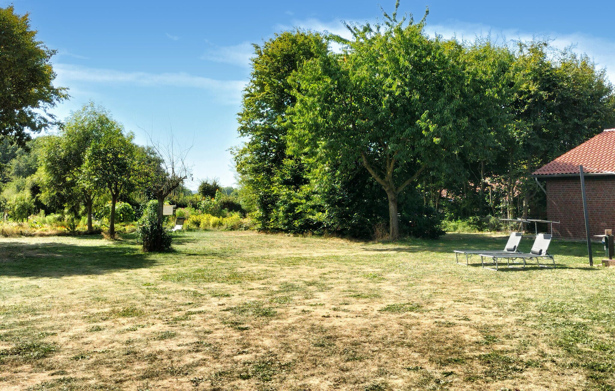 A grassy outdoor area with a brick building, two lounge chairs, and a large tree.