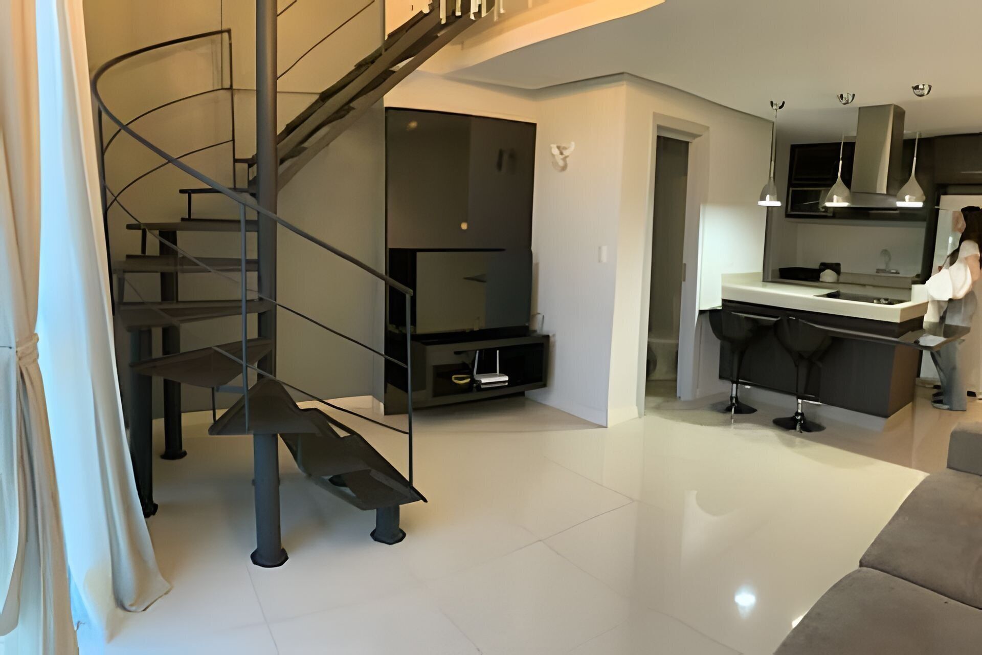 A modern interior with a spiral staircase, a flat-screen TV, and a kitchen area with bar stools.