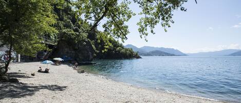 A pebble beach with a rocky outcrop and a clear view of the lake and distant mountains.