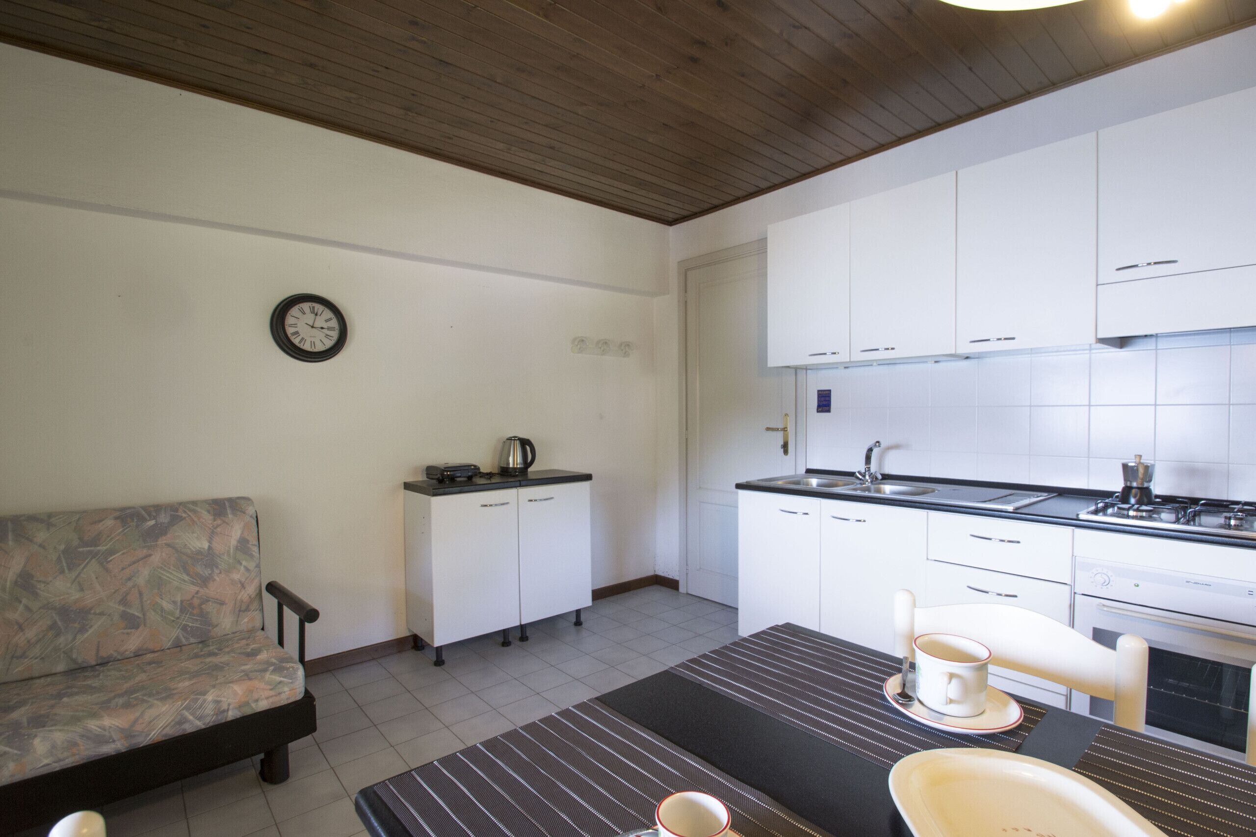 A compact kitchen with white cabinets, a dining table with a cup, and a sofa.