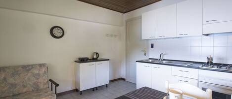 A compact kitchen with white cabinets, a dining table with a cup, and a sofa.