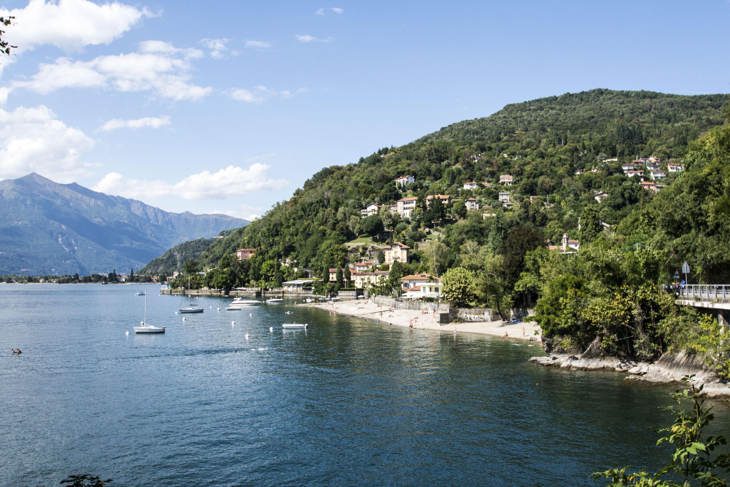 A lakeside town with buildings on a hillside, boats on the water, and a clear sky.