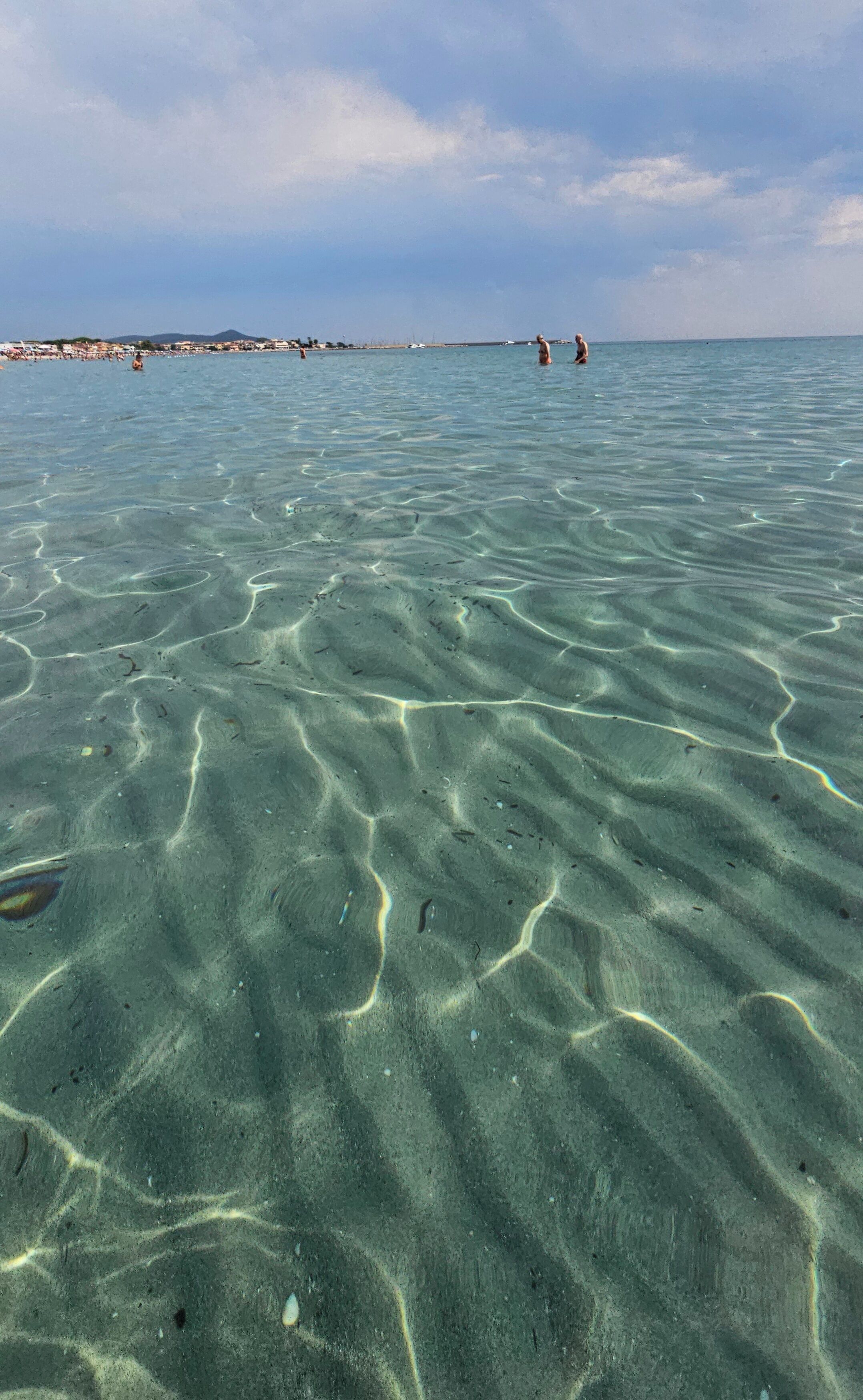 Een strand met helder ondiep water en een verre kustlijn met gebouwen.