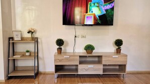 Un salon moderne avec un meuble de rangement en bois pour l’équipement audiovisuel, un téléviseur fixé au mur et une petite étagère ornée d’objets décoratifs.