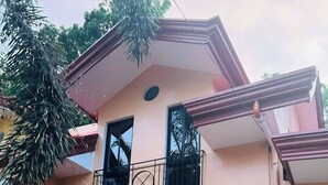Une maison à deux étages avec un balcon, une porte en bois et une fenêtre ornée d’une croix.